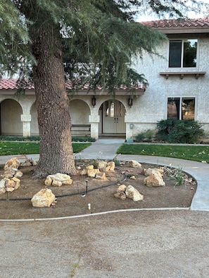 Un edificio con fachada de piedra, un árbol grande y un jardín de rocas al frente.