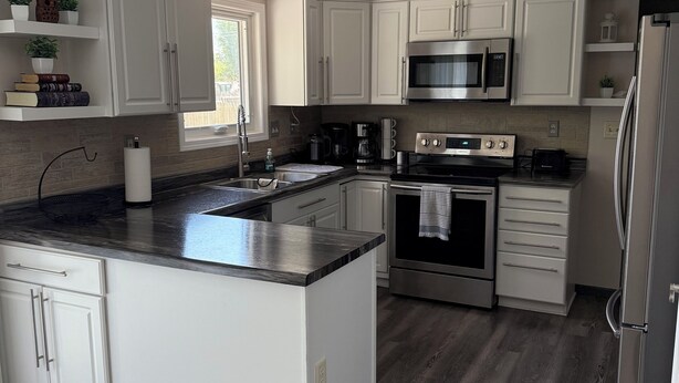 A modern kitchen with white cabinetry, a central island, stainless steel appliances, and a dark wood floor. - Charming 3 Bedroom 2.5 bathroom finished basement, Huge yard and Charcoal grill (Baraboo)