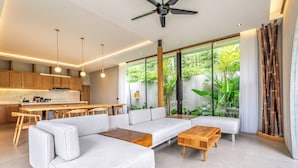 A modern living room with a sofa, coffee table, and dining area. - Titi House Villa By Betterplace (Ubud)