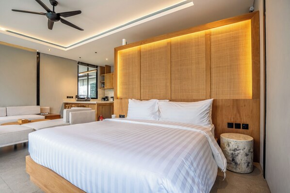 A modern hotel room with a large bed, a ceiling fan, a wooden headboard, a round side table, and a seating area with a sofa and chairs. - Titi House Villa By Betterplace (Ubud)