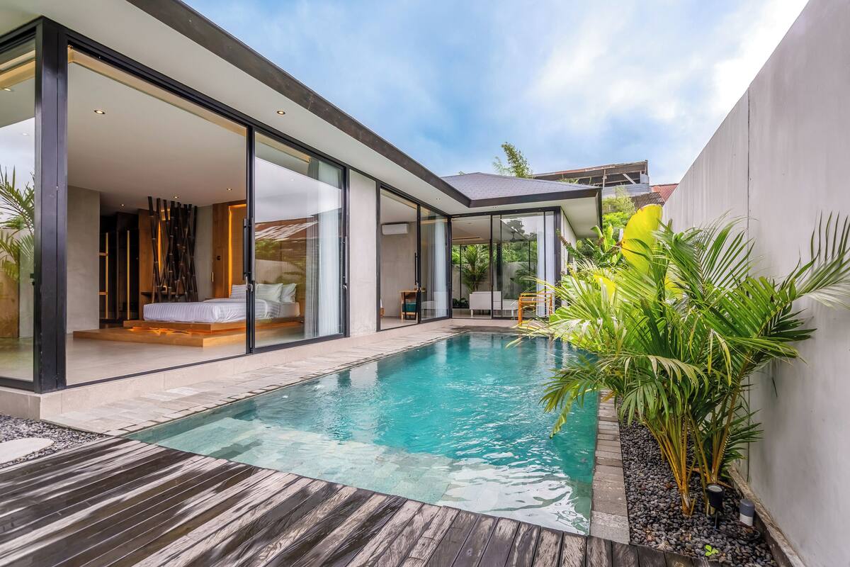 Ein modernes Haus mit einer gläsernen Veranda, einem Schwimmbad und einer Holzterrasse.