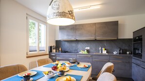 Una cocina moderna con armarios oscuros, una mesa de comedor dispuesta con platos de comida y una lámpara colgante.