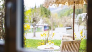 Una mesa con una botella, vasos, una silla y un parasol de paja en un jardín.