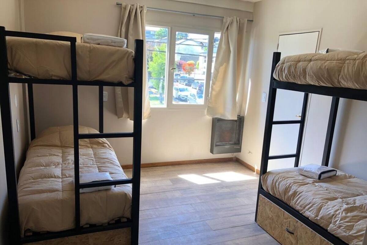 Une chambre de dortoir avec des lits superposés, une fenêtre avec des rideaux et un radiateur.