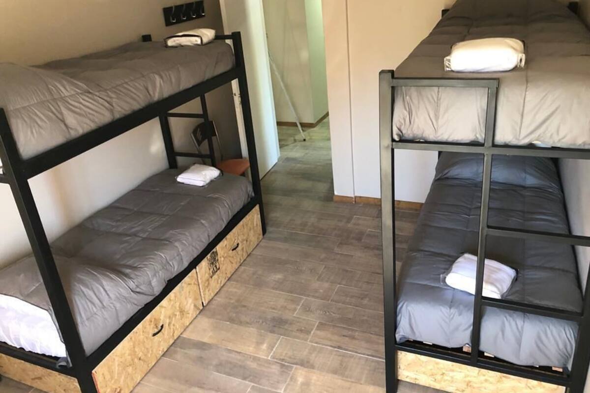 Une chambre avec deux lits superposés, chacun étant équipé d’un matelas et d’oreillers. On trouve une armoire en bois sous l’un des lits.
