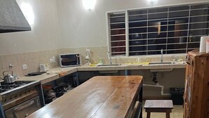 Cocina con una isla de madera larga, estufa, microondas y pileta. Hay taburetes y un mueble.