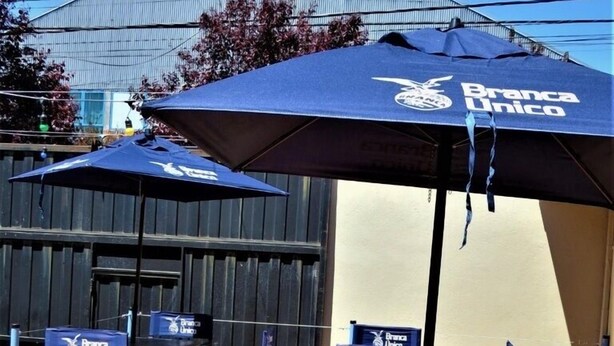 Un área de estar al aire libre con sombrillas azules y sillas con la marca 'Branca Unico'.