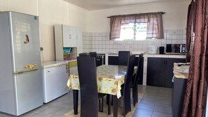 Cuina compacta amb nevera, microones i fogó. Hi ha una taula de menjador amb caires i una finestra amb cortines.
