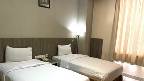 A hotel room with two single beds, a bedside table with a lamp, and a window with curtains. - Lynt Hotel Makassar (Makassar)