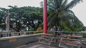 An outdoor seating area with benches and a red pole, surrounded by greenery and trees. - Lynt Hotel Makassar (Makassar)