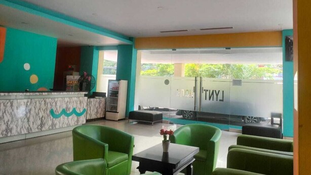 A hotel lobby with a reception desk, green seating area, and a view of the outside. - Lynt Hotel Makassar (Makassar)