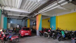 A parking garage with multiple motorcycles and a red car. - Lynt Hotel Makassar (Makassar)