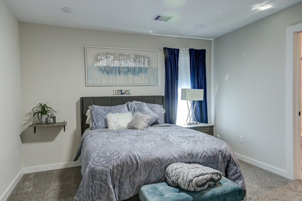 A bedroom with a bed, a bedside table, a lamp, and a wall-mounted artwork.