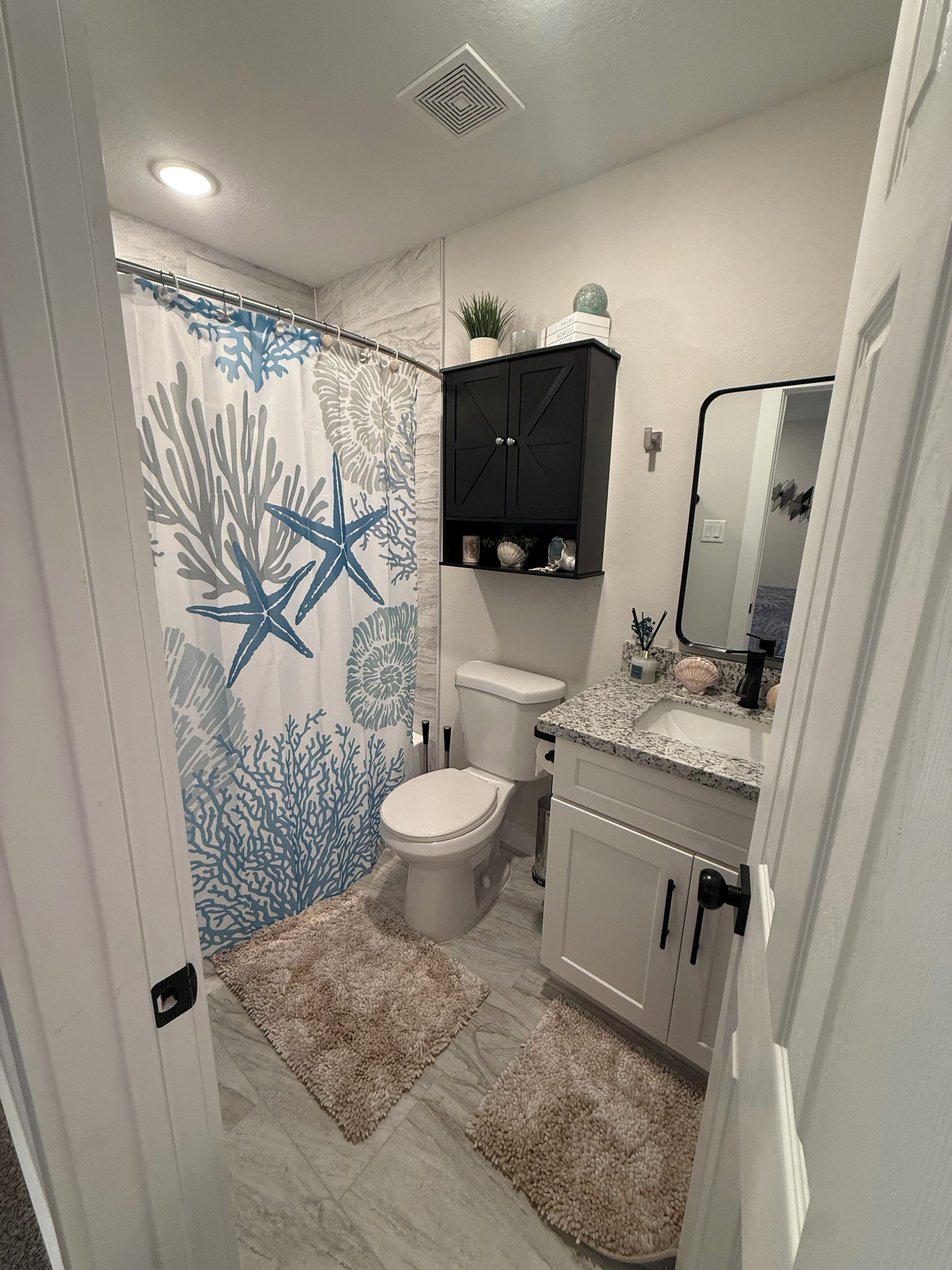 Une salle de bain équipée de toilettes, d’un lavabo et d’un rideau de douche orné de motifs d’étoiles de mer.
