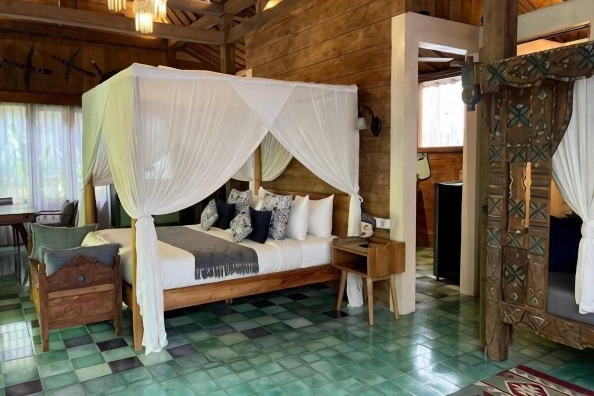 A four-poster bed with a canopy, a wooden floor, and a small bedside table.