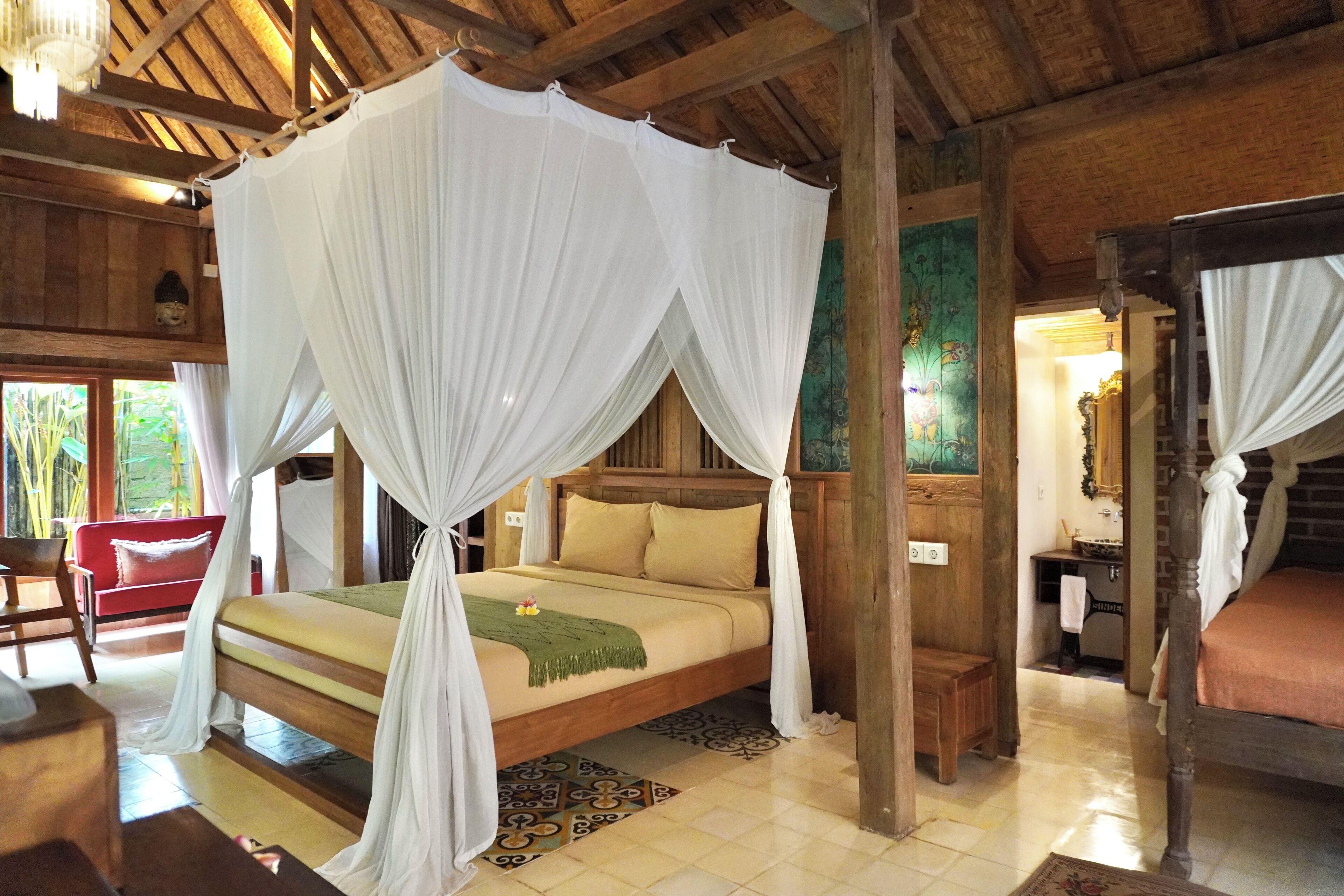A room with a bed under a canopy, wooden walls, a red chair, and a small table.