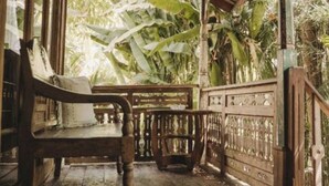 A wooden porch with a bench, a railing, and a view of tropical foliage. - Umakayu Joglo Villa Bali Boutique Hotel (Canggu)