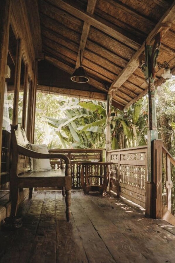 A wooden porch with a bench, a railing, and a view of tropical foliage.