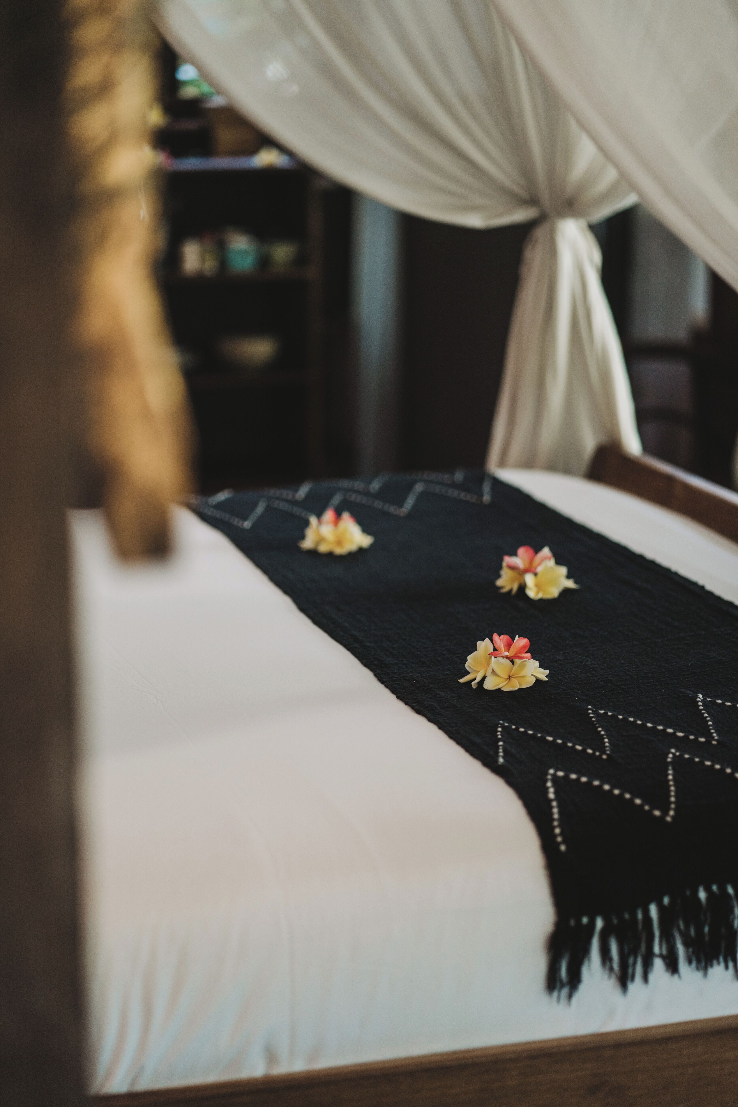 Cama com colcha preta e almofadas decorativas, um dossel acima e cabeceira de madeira.
