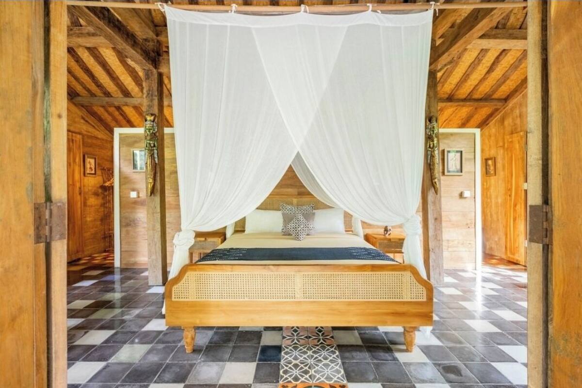 A wooden room with a bed under a white canopy, checkered floor, and wooden walls.