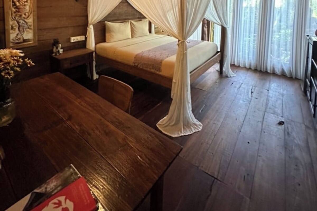 A rustic wooden room with a bed under a canopy, a wooden table, and a painting on the wall.