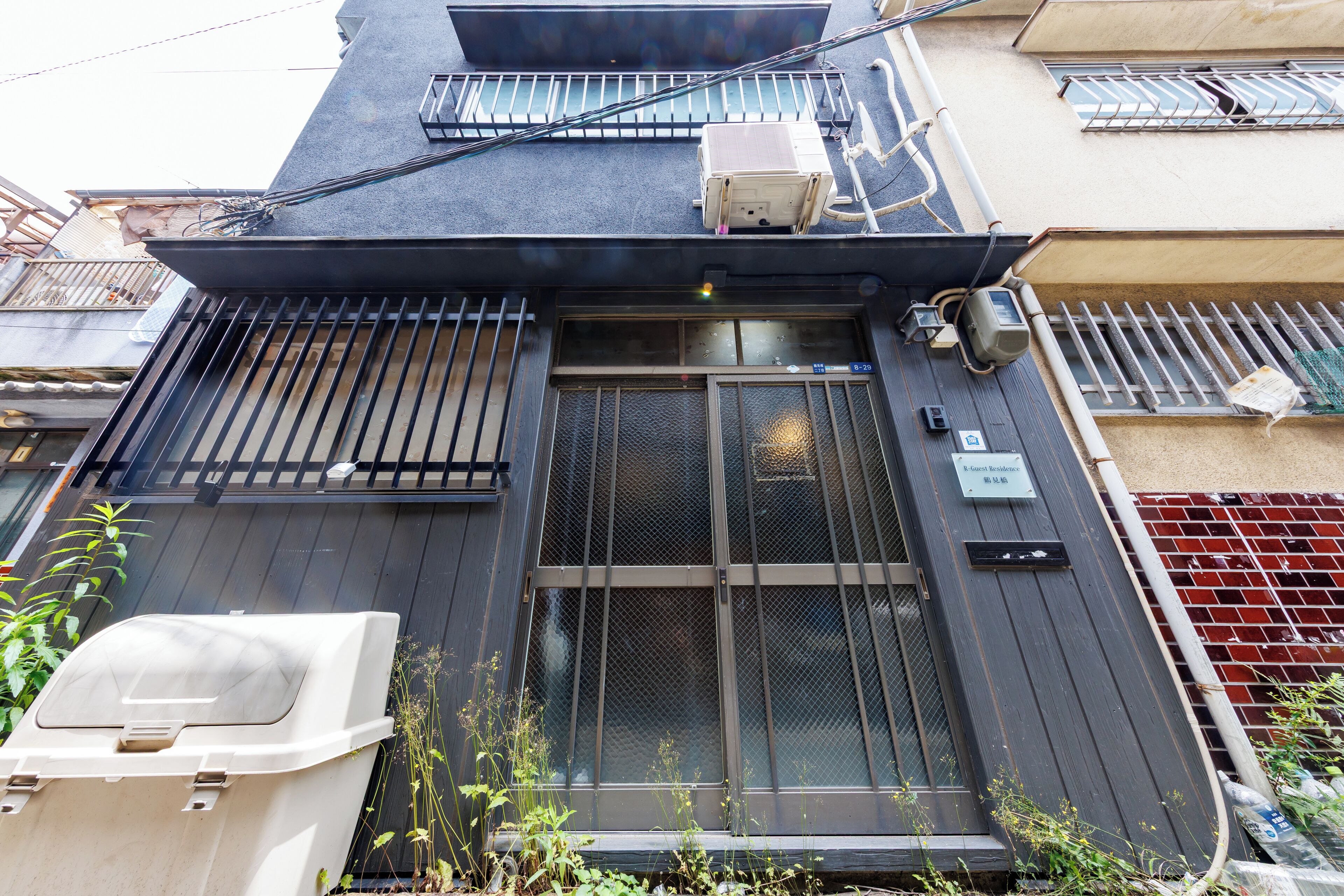 A building with a dark facade, a metal gate, and a small air conditioning unit on the roof.