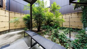 A covered outdoor area with a bench, bamboo fencing, and greenery. - R-Guest Residence Tsurumibashi (Osaka)