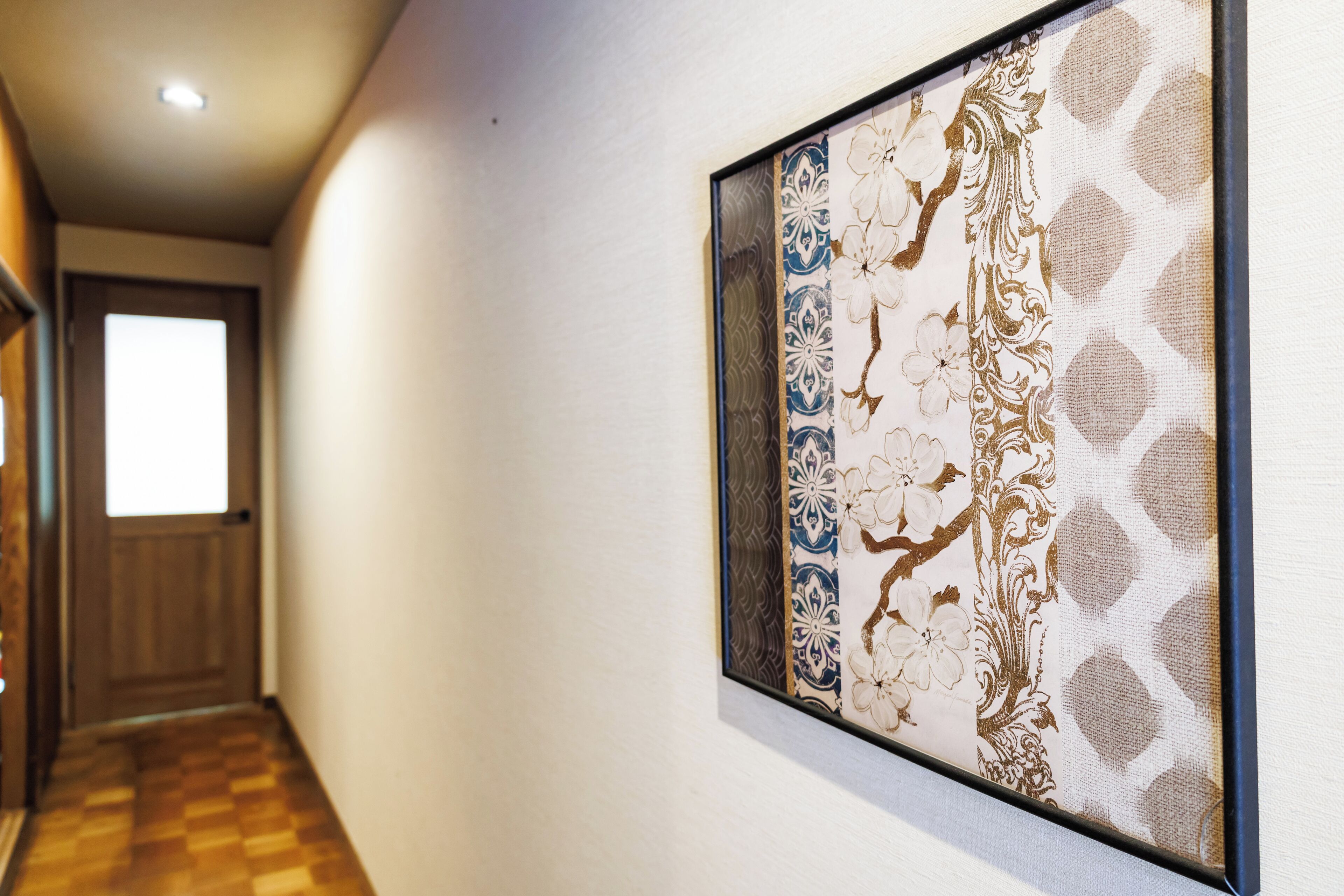 Un pasillo con una obra de arte decorativa en la pared, una puerta de madera al final y un suelo a cuadros.