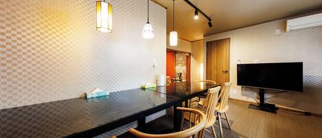 A modern kitchen with a black countertop, wooden chairs, pendant lights, and a flat-screen TV.