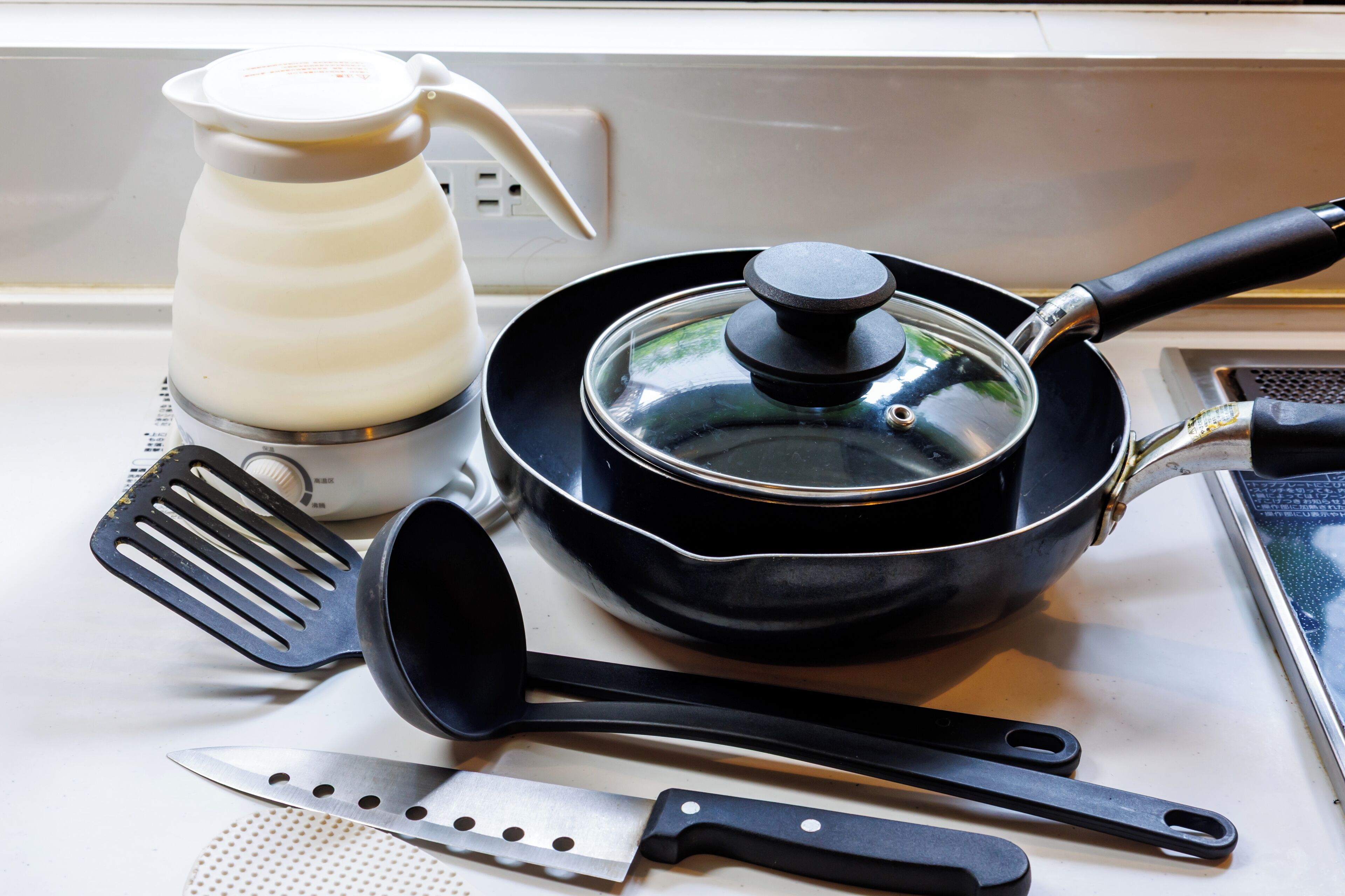 A kitchen counter with a coffee maker, a frying pan, a spatula, a ladle, and a knife.