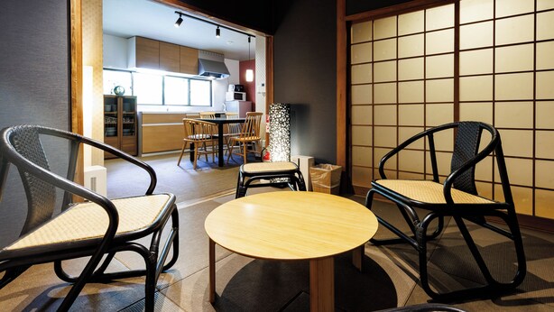 A traditional Japanese-style room with tatami flooring, a low wooden table, and black woven chairs. - R-Guest Residence Tsurumibashi (Osaka)