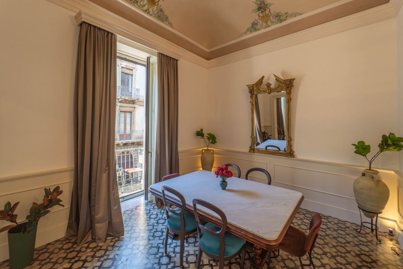 Un coin repas comprenant une table, des chaises, un vase avec des fleurs, un miroir et une vue sur un balcon.