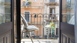 Un balcón con una silla y una mesita, con vistas a un edificio con balcones y ventanas.