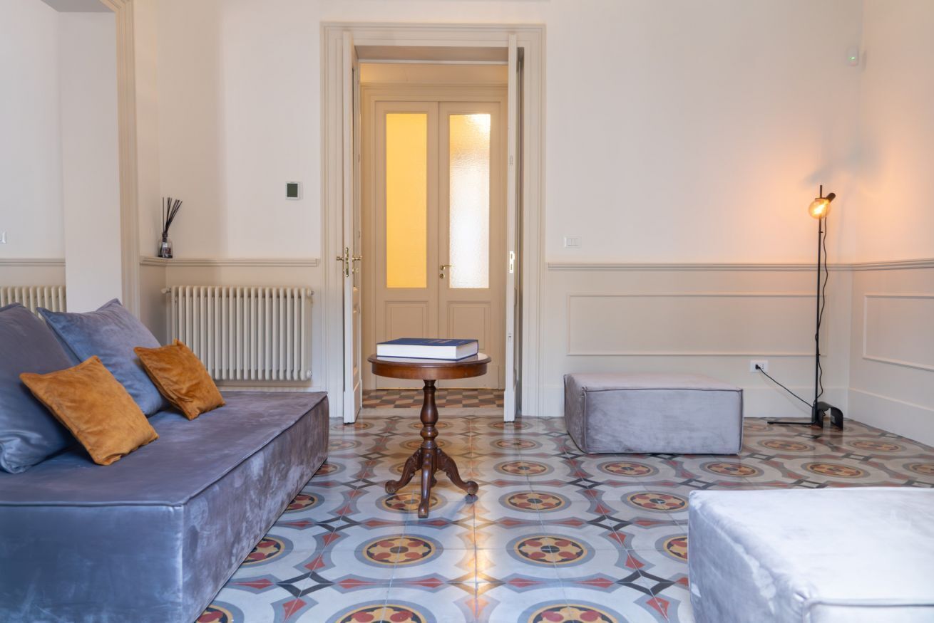 A room with a blue sofa, a small round table with a book, a patterned floor, and a door leading to another room.