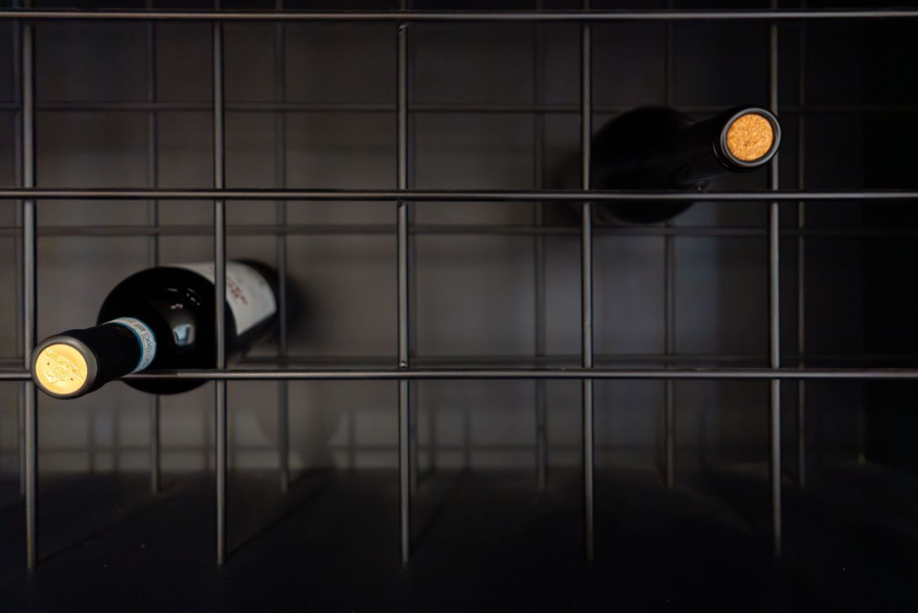 Two bottles of wine on a wire shelf in a dark room.