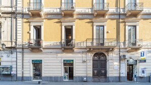 Un edificio de varios pisos con balcones, una entrada central con un gran portón y locales comerciales en la planta baja.