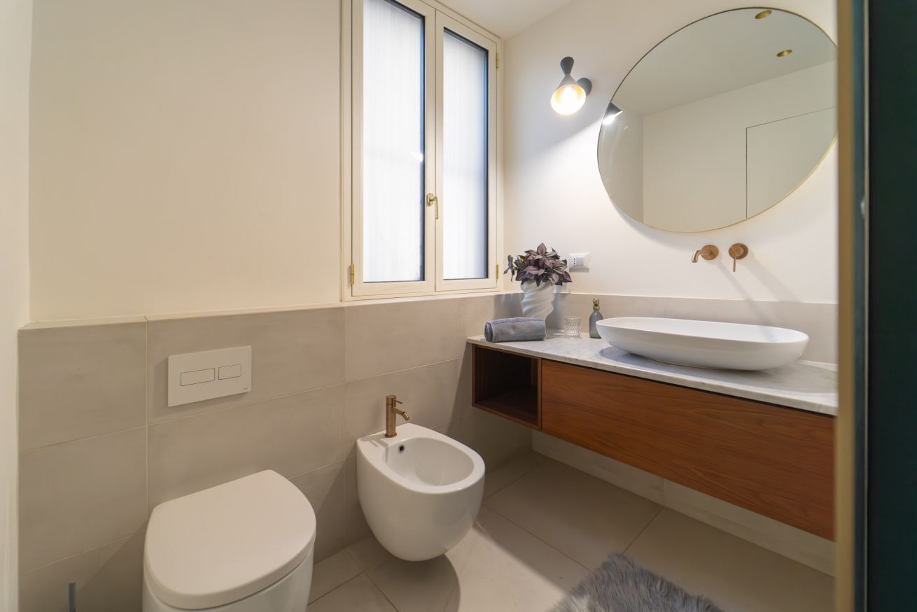 Een moderne badkamer met toilet, bidet, wastafel en een grote spiegel.