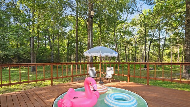 Eine Holzterrasse mit Pool, umgeben von einem Holzzaun und Bäumen.