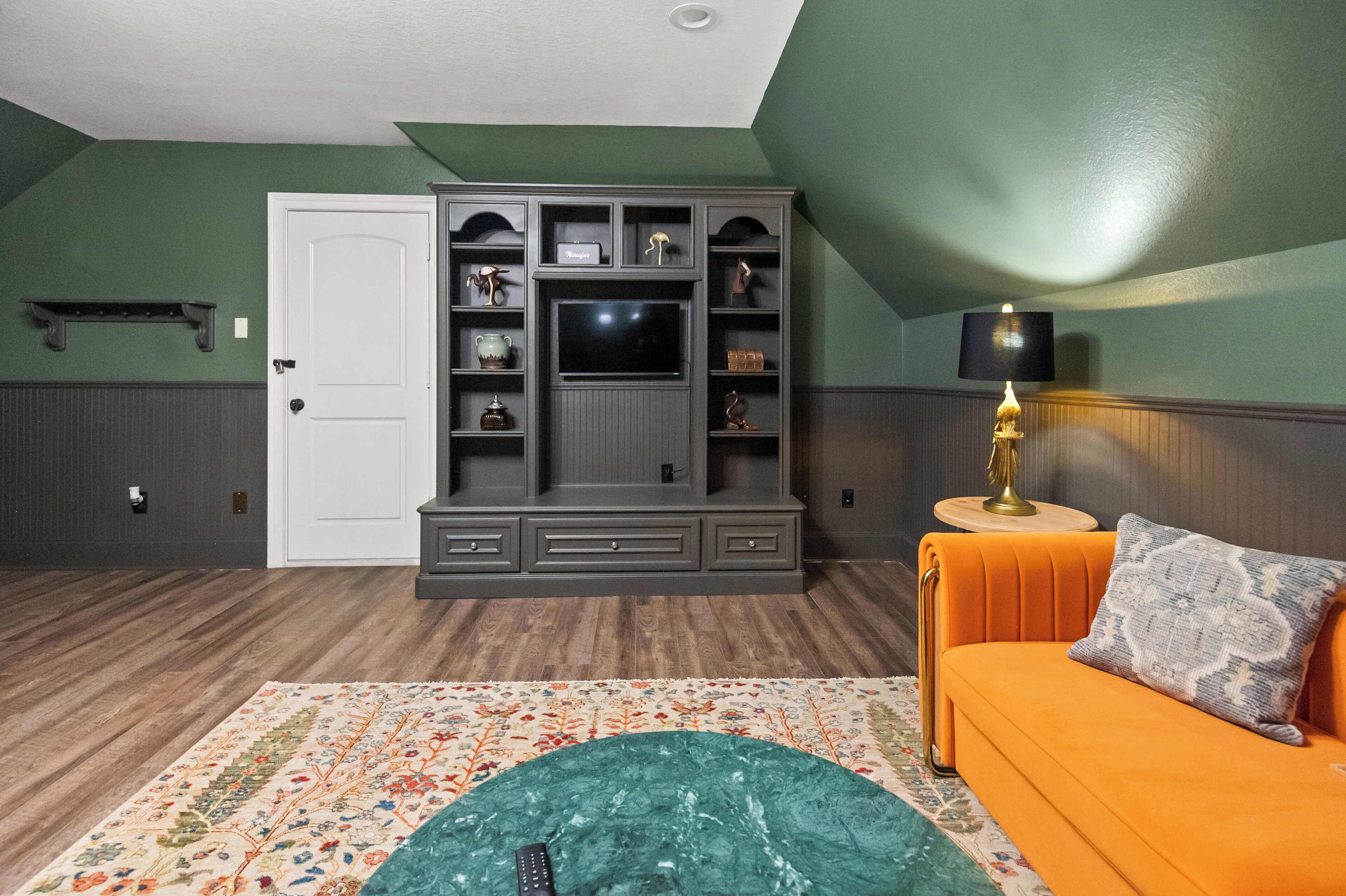 Un salon avec un meuble de rangement pour appareils électroniques de couleur gris foncé, un téléviseur, une petite table avec une lampe et un canapé avec des coussins.