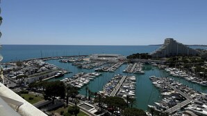 Un port de plaisance où sont amarrés de nombreux bateaux, un grand bâtiment doté d’un toit incurvé et une vue dégagée sur la mer.
