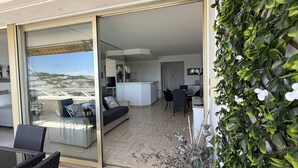 Un appartement moderne doté d’une porte vitrée donnant sur un balcon, d’un espace de vie avec un canapé et des fauteuils, d’une cuisine et d’un coin repas.
