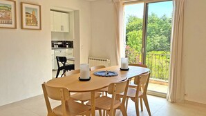 A dining area with a wooden table and chairs, a kitchen in the background, and a balcony with a view of greenery. - Apartment for 6people - Air conditioning - Litlle sea view - Wifi - Sainte Maxime (STE MAXIME)