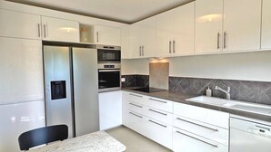 A modern kitchen with white cabinets, a built-in oven, a microwave, and a sink. - Apartment for 6people - Air conditioning - Litlle sea view - Wifi - Sainte Maxime (STE MAXIME)
