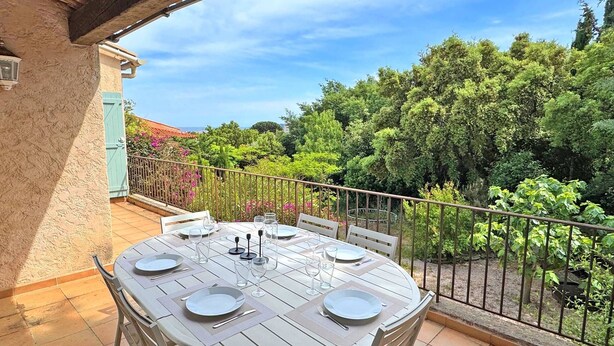 A round outdoor table set for dining with chairs, a railing, and a view of a garden with trees and shrubs. - Apartment for 6people - Air conditioning - Litlle sea view - Wifi - Sainte Maxime (STE MAXIME)