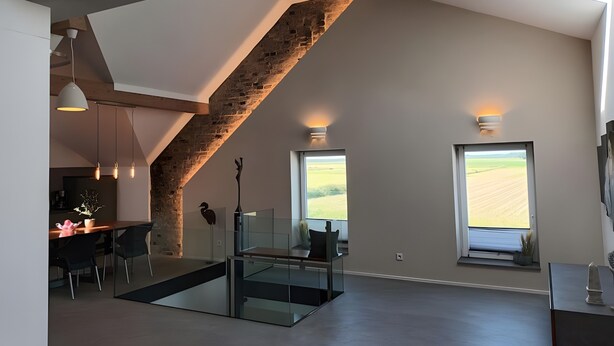A modern interior with a loft-style staircase, a dining area, and large windows offering views of the countryside.