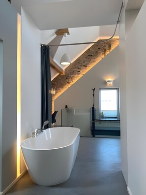Une salle de bain moderne avec une baignoire sur pieds, un puits de lumière et un mur en briques.