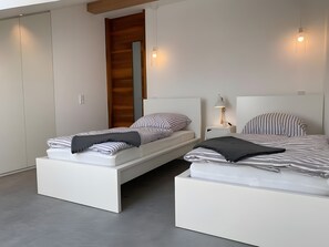 Une chambre moderne avec deux lits, un mur recouvert de panneaux en bois et une armoire blanche.
