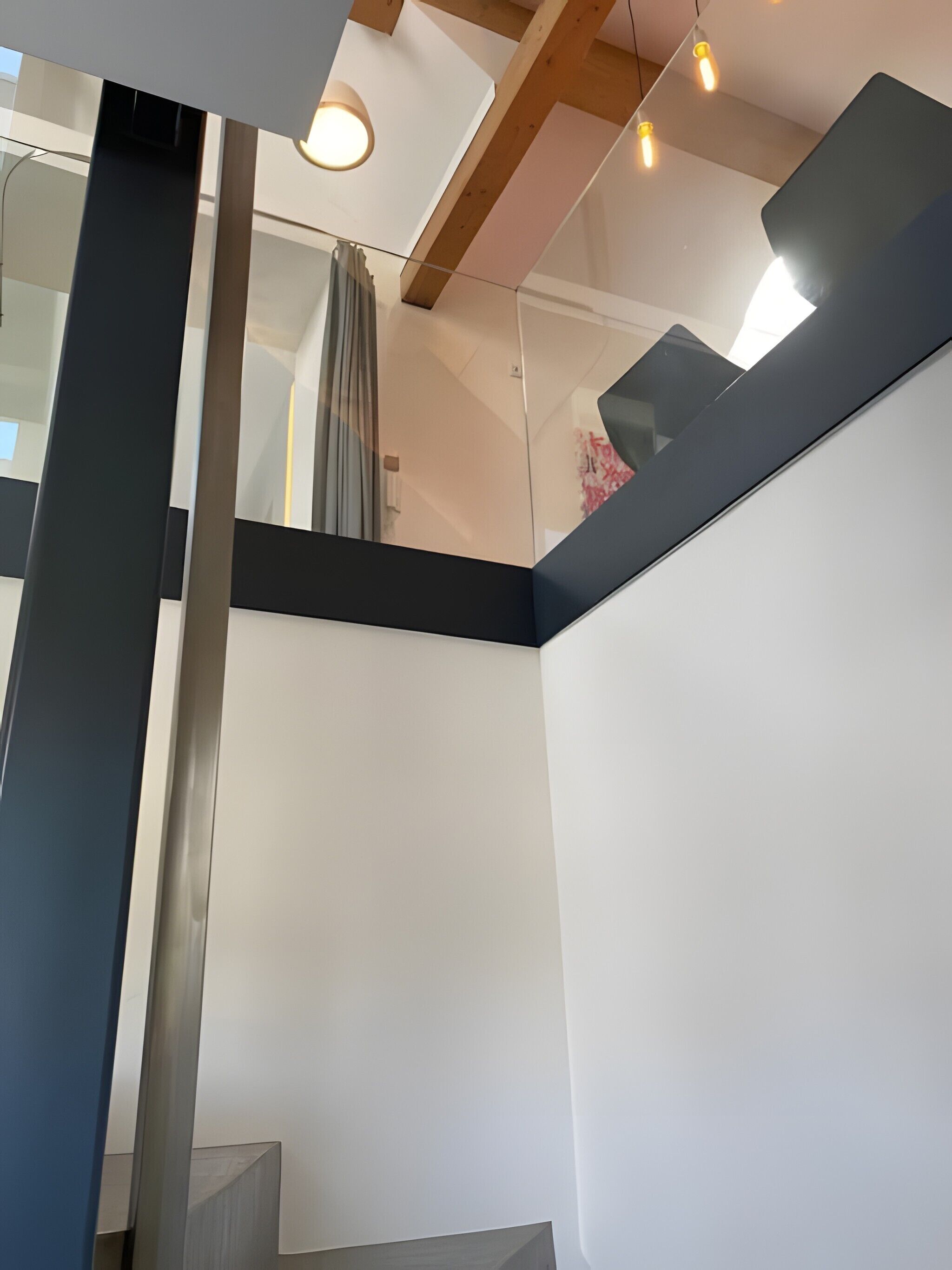 A modern interior with a staircase, glass walls, and exposed wooden beams.