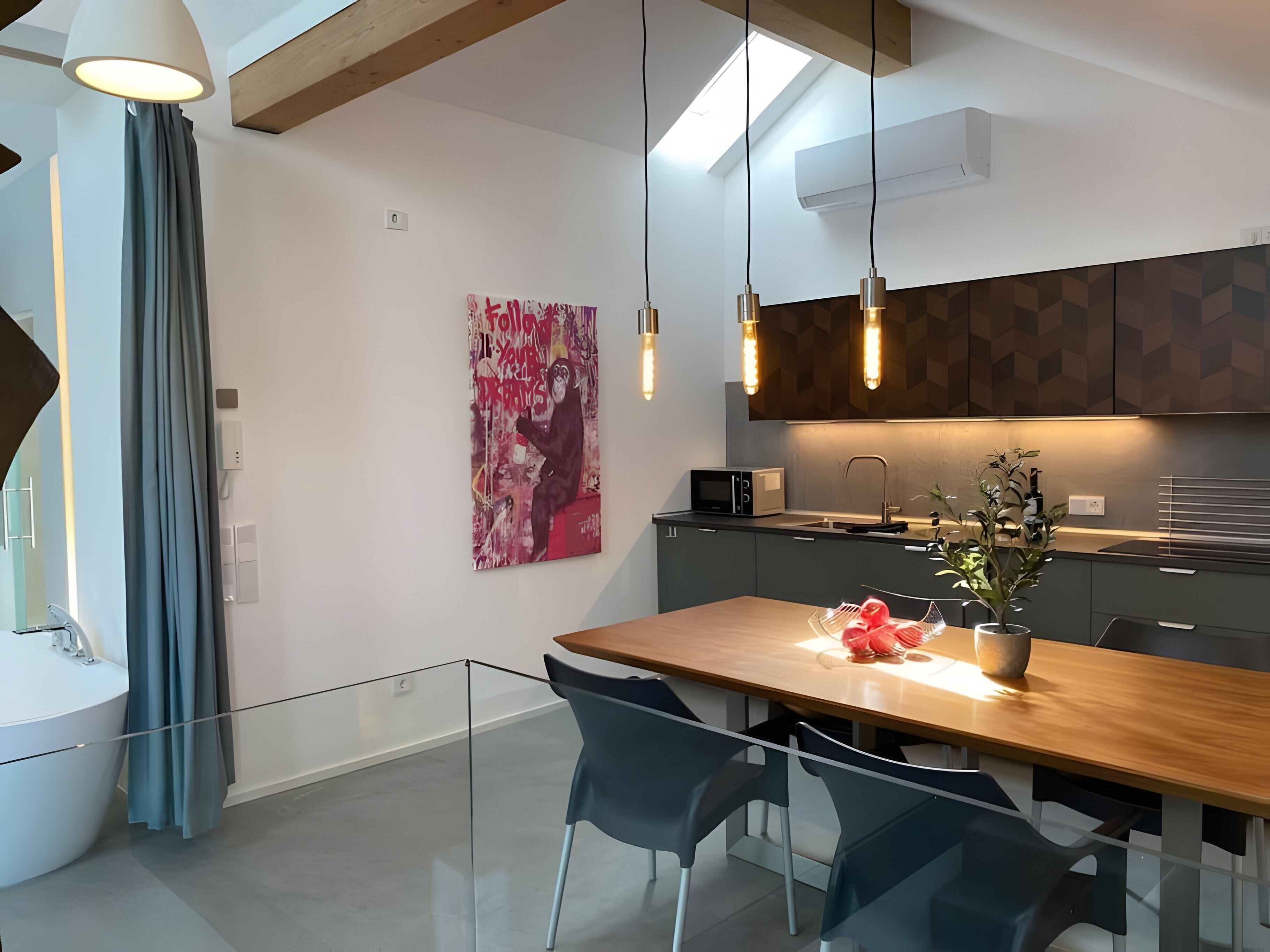 Een moderne keuken met een eethoek, met een houten tafel, stoelen, hanglampen en een magnetron.