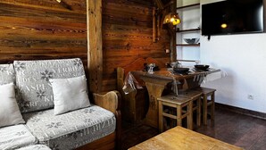 Une pièce chaleureuse avec un mur en bois, un canapé, une table à manger et un téléviseur fixé au mur.